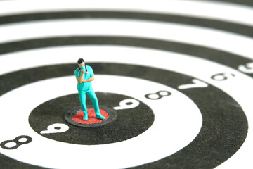 Miniature people toy figure photography. A men doctor or nurse thinking in the middle dartboard...