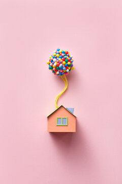 Papercraft house model with balloons on pink background