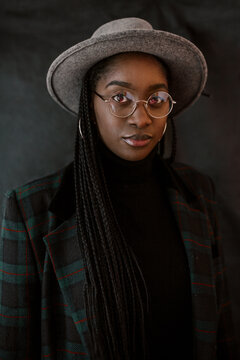 Dark skin girl in a hat glasses looking at the camera coat and braids