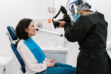 Dentist with mask and protective clothing, taking a photo of his patient.