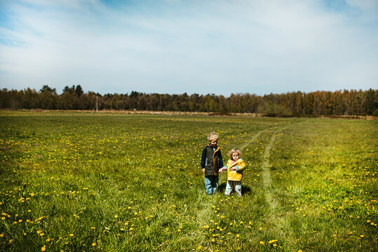 Brother and sister standing in a field with yellow flowers