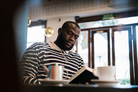 Black man sitting in a coffee shop reading a book.