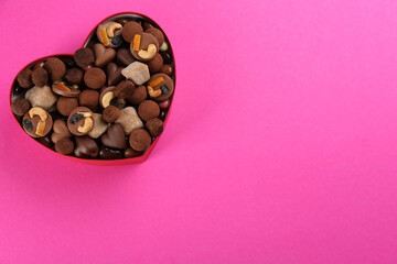 Different delicious chocolate candies in heart shaped box on pink background, top view. Space for text