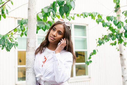 Pacific Islander woman speaking on smartphone near tree