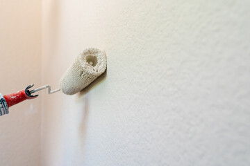 Roller brush with white paint on a wall.