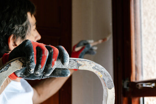 Worker's hand with gloves painting a wall.