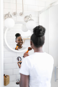 Young woman doing her make up in bathroom while looking herself in the mirror