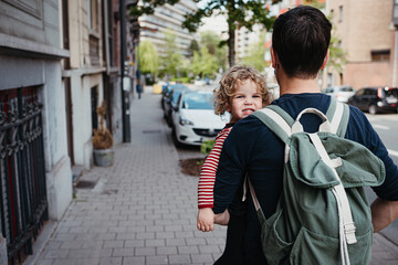 Dad with green backpack walking in the city while holding his daughter