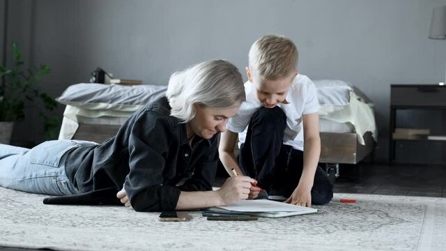 A Young Mother and a Baby Boy Are lying on the Floor, Drawing with Felt-Tip Pens on Paper, Talking and Having Fun