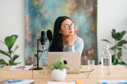 Dreamy Asian woman preparing for recording podcast in modern studio