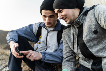 Portrait of two adult men male migrants sitting outdoor in rural environment in cold day checking...