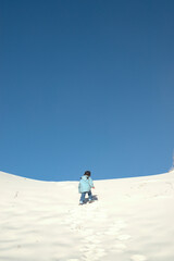 Fototapeta na wymiar 青い空と白い砂丘を登っていく子供