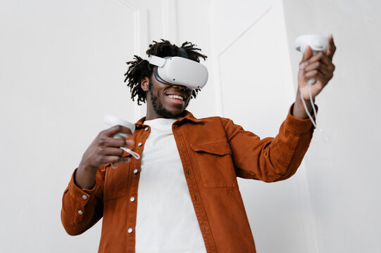 Happy black guy playing VR videogame against white wall