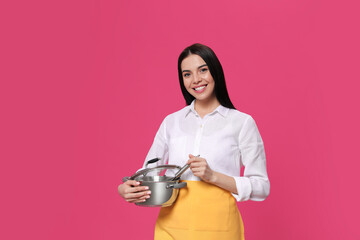 Young housewife with pan on pink background