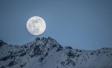 Full moon rising over snowy mountain range in the alps