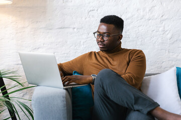 Young businessman sitting at the couch in the office using his laptop