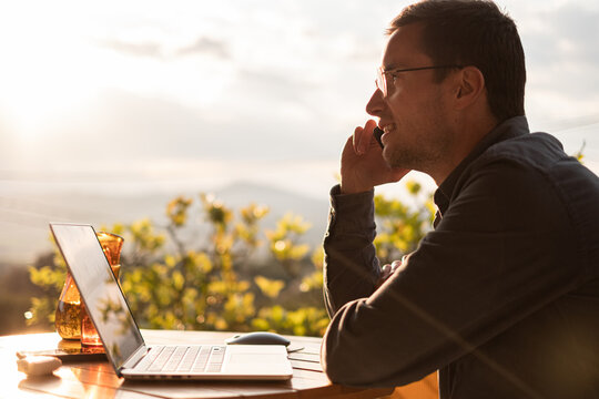 Freelancer man talking on the phone while remote Working On A Laptop Outdoors