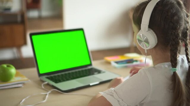 Child in headphones look at laptop green screen and talk on video call lesson at home Spbd. Webcam