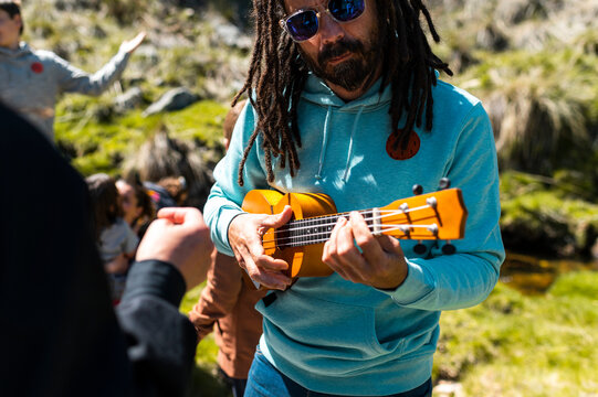 Young man with dreadlocks playing the ukulele in nature