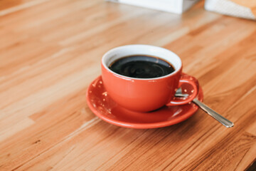Hand holding hot cup of coffee on wood table. Morning cup of coffee. Hipster tone. Selective focus, blur background.