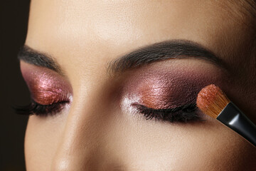 Applying dark eye shadow with brush onto woman's face, closeup. Beautiful evening makeup - obrazy, fototapety, plakaty