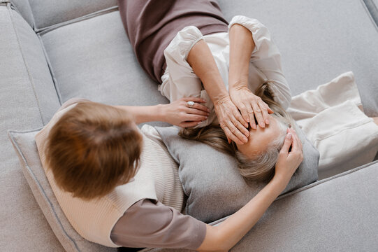 Adult daughter comforting upset mature mother on sofa