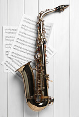 Beautiful saxophone and note sheets on white wooden background, flat lay