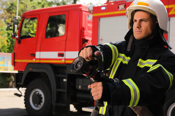 Fototapeta premium Firefighter in uniform with high pressure water jet near fire truck outdoors