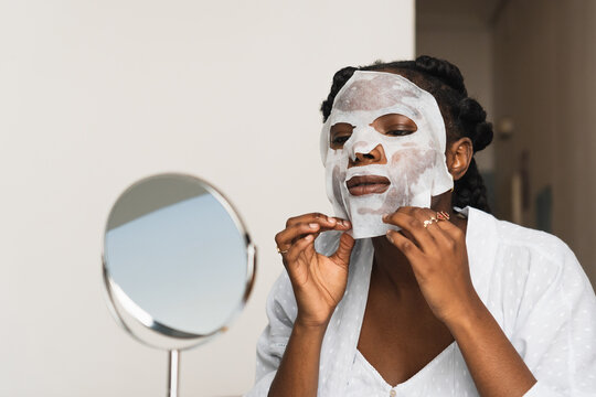 Black woman applying sheet mask on face