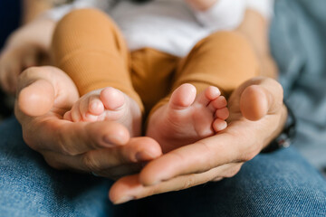 Family lifestyle, close up image of a young millennial father holding his baby's legs in his hands 