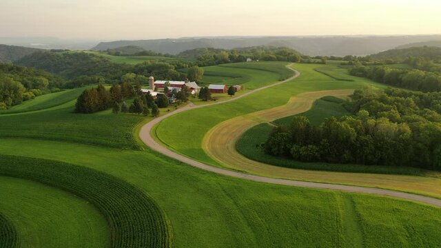 Midwest USA Rural farm scene at sunrise sunset sunlight. Rural landscape with agricultural fields, rows of corn and wheat, farm house. American Countryside. Aerial view, sunny sky, summer.