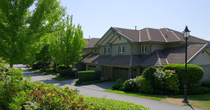 Establishing shot of two story stucco luxury house with garage door, big tree and nice landscape in Vancouver, Canada, North America. Day time on June 2021. ProRes 422 HQ.