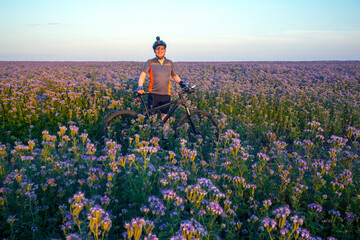 Happy cyclist stands with a bicycle in a blooming field of flowers