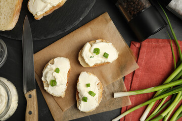 Bread with cream cheese and green onion on black table, flat lay