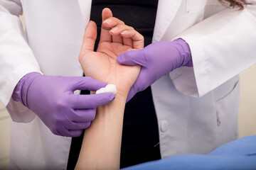 Médico limpiando con algodón el área del brazo donde aplicará un tratamiento médico en clínica de salud - obrazy, fototapety, plakaty