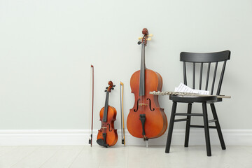Stringed and wind musical instruments near white wall indoors, space for text