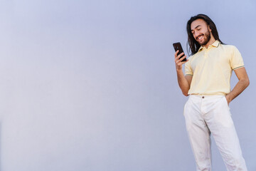 young hispanic latino male with long hair, college student chatting on his smart phone while laughing, copy space, gray wall background