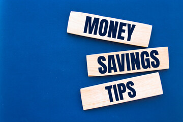block with word 'money' on top of a blocks with words 'money savings tips'. Beautiful wooden table, blue background. Copy space. Business concept.