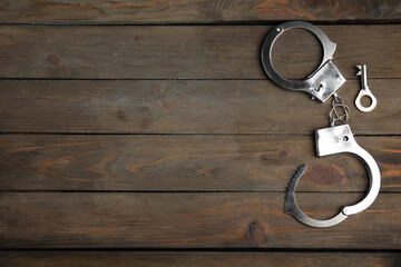 Classic chain handcuffs with key on wooden table, flat lay. Space for text