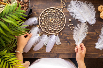 Top view female craftsman hands creating traditional dreamcatcher choosing material at workshop