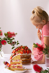 A cute girl is sitting on the table with a strawberry cake.Strawberry cake.