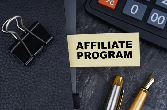 On the table is a calculator, a pen and a notebook with a bookmark on which it is written - AFFILIATE PROGRAM