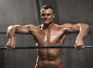 Fototapeta na wymiar Smiling male athlete doing pull ups on bar during cross fit training in gym