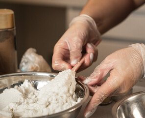 Hands with transparent gloves handling butter cream in a metal bowl.