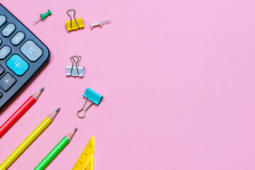 Back to school concept. School and office supplies on a pink background. Multi-colored stationery and black calculator