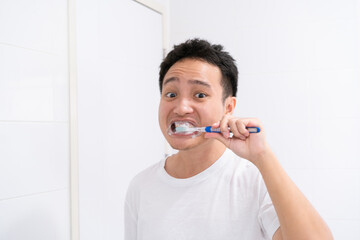 Asian young man in white shirt brushing his tooth in front of the mirror in the morning.