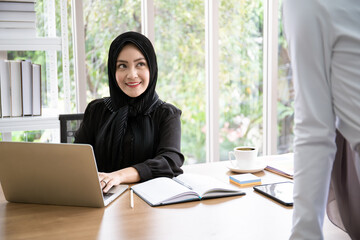 Obraz na płótnie Canvas Cheerful Asian muslim businesswomen talking together in their workplace during the break. 