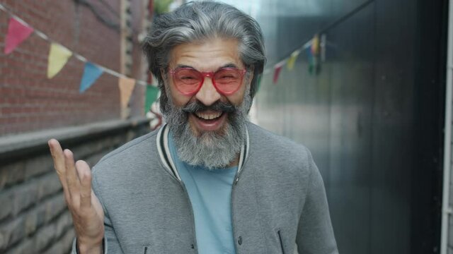 Slow motion portrait of cheerful mature man in stylish sun glasses laughing outside against urban background. Happiness and emotions concept.