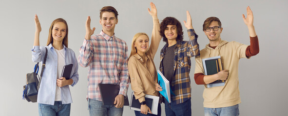 Group of active students in casual clothes and with textbooks in hands raise their hands while...