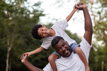 afro boy with his father in the park on his neck